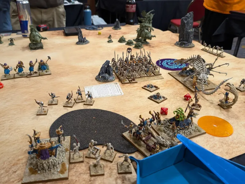 Tomb Kings skeleton regiments and a bone dragon squaring off against green Lizardmen across a sandy tournament table.
