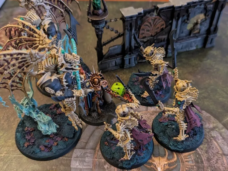 Painted Bonereaper miniatures on a gaming board: a winged skeletal construct and bone-armoured warriors closing in on a lone gold-armoured Stormcast hero.