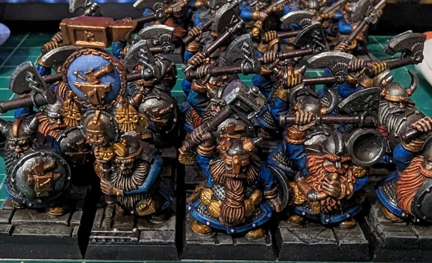Ranked-up dwarf miniatures in blue and gold with axes over their shoulders, painted in an older studio style.