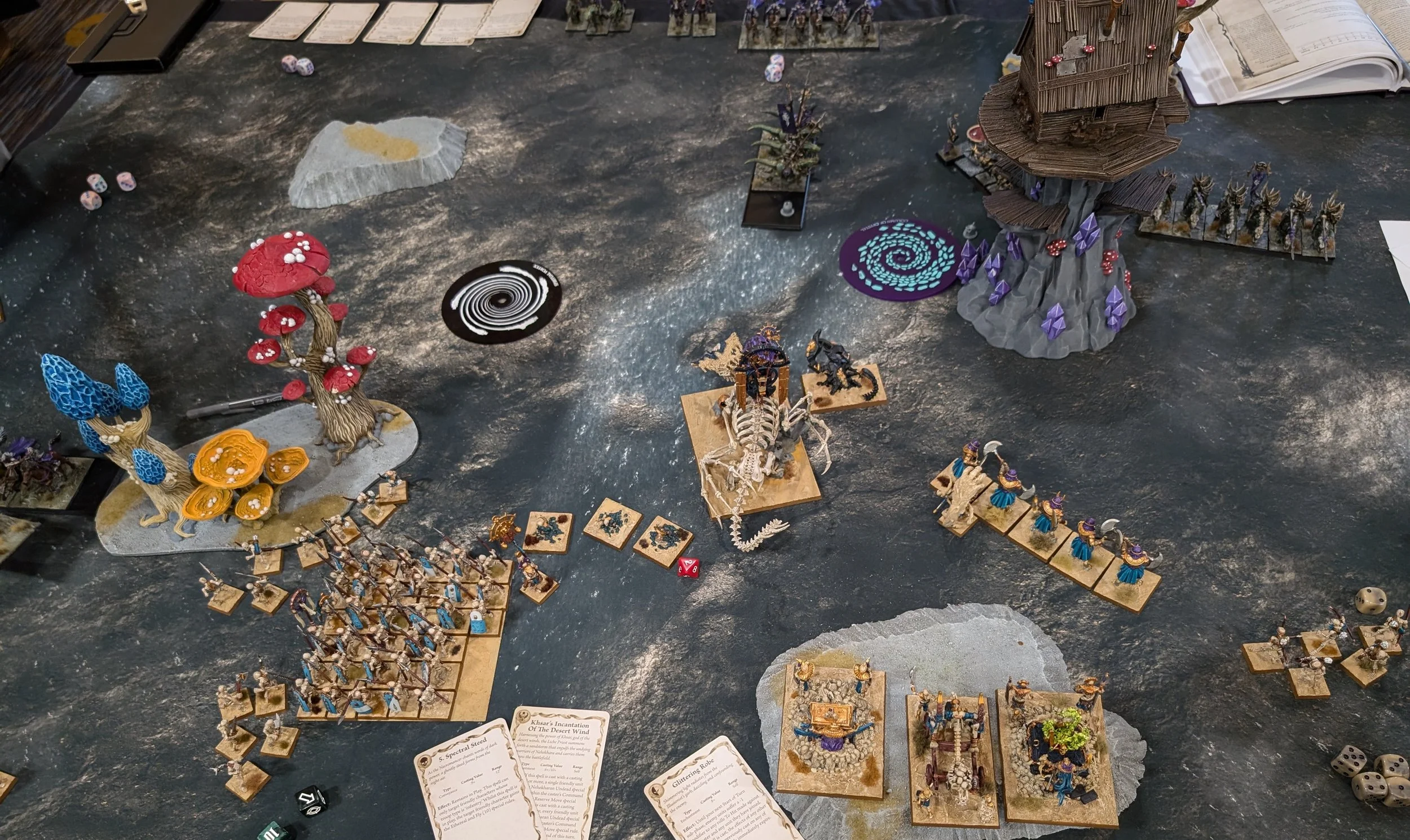 Dark grey gaming table with giant mushroom woods and a crystal outcrop; a Tomb Kings bone dragon and skeleton regiments face Dark Elf units across the middle.