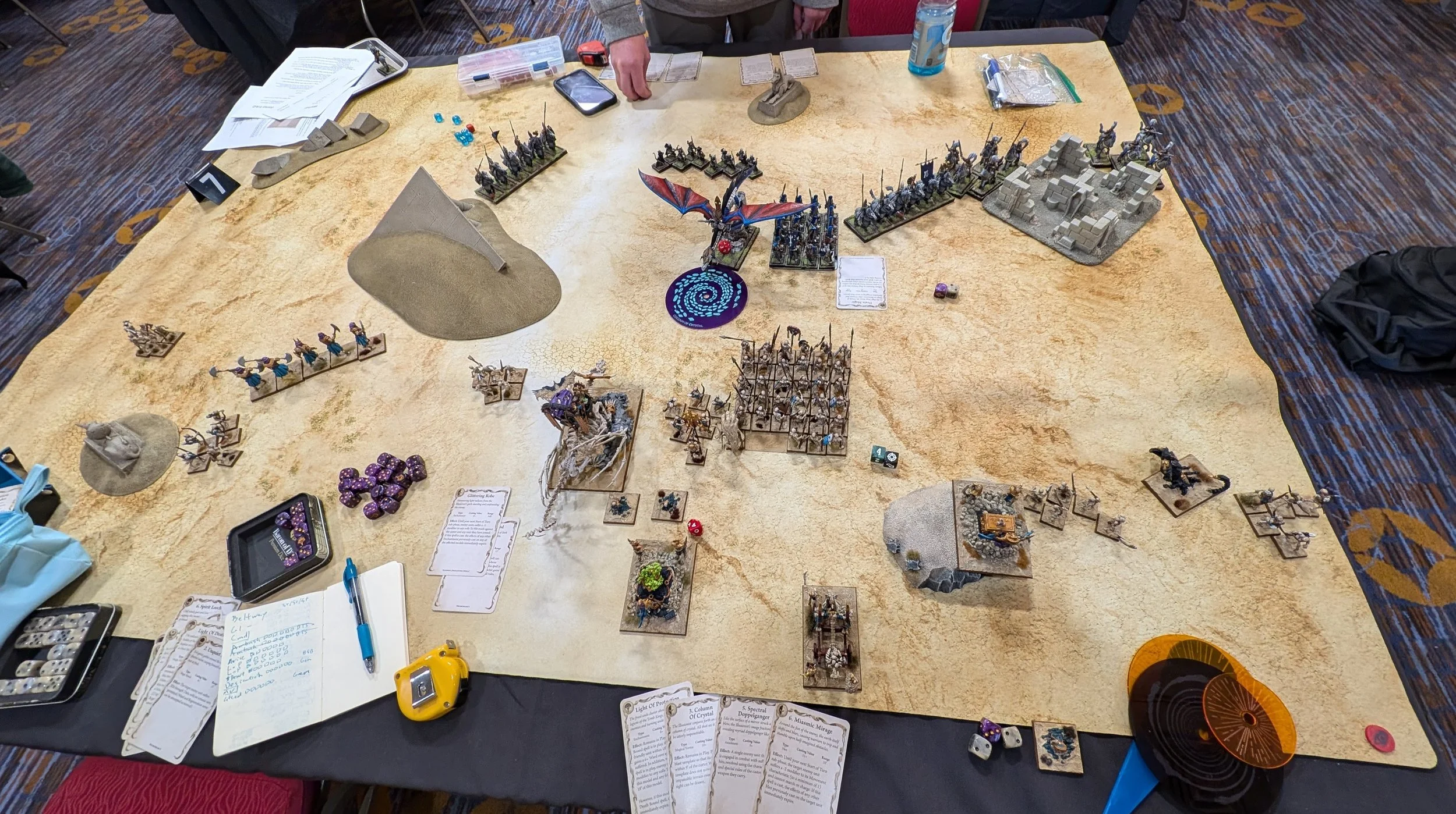 The same desert table later on: a blue Column of Crystal marker sits between the High Elf dragon and the Tomb Kings' skeletal bone dragon, with skeleton blocks advancing up the middle.