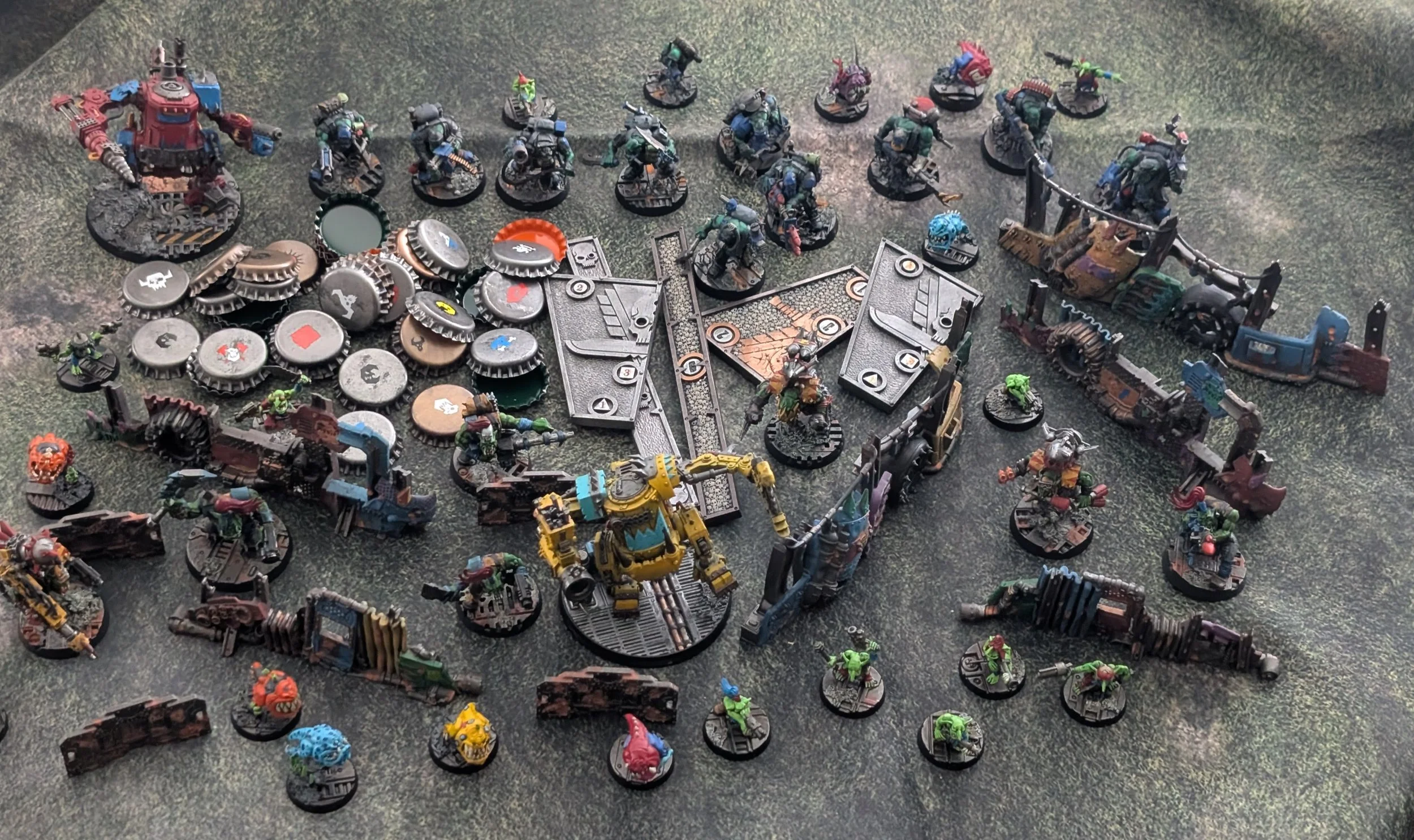 The author's Space Gits collection laid out: dozens of ork miniatures and a yellow mech, plus scatter terrain, objective markers, and a pile of bottle caps used as tokens.