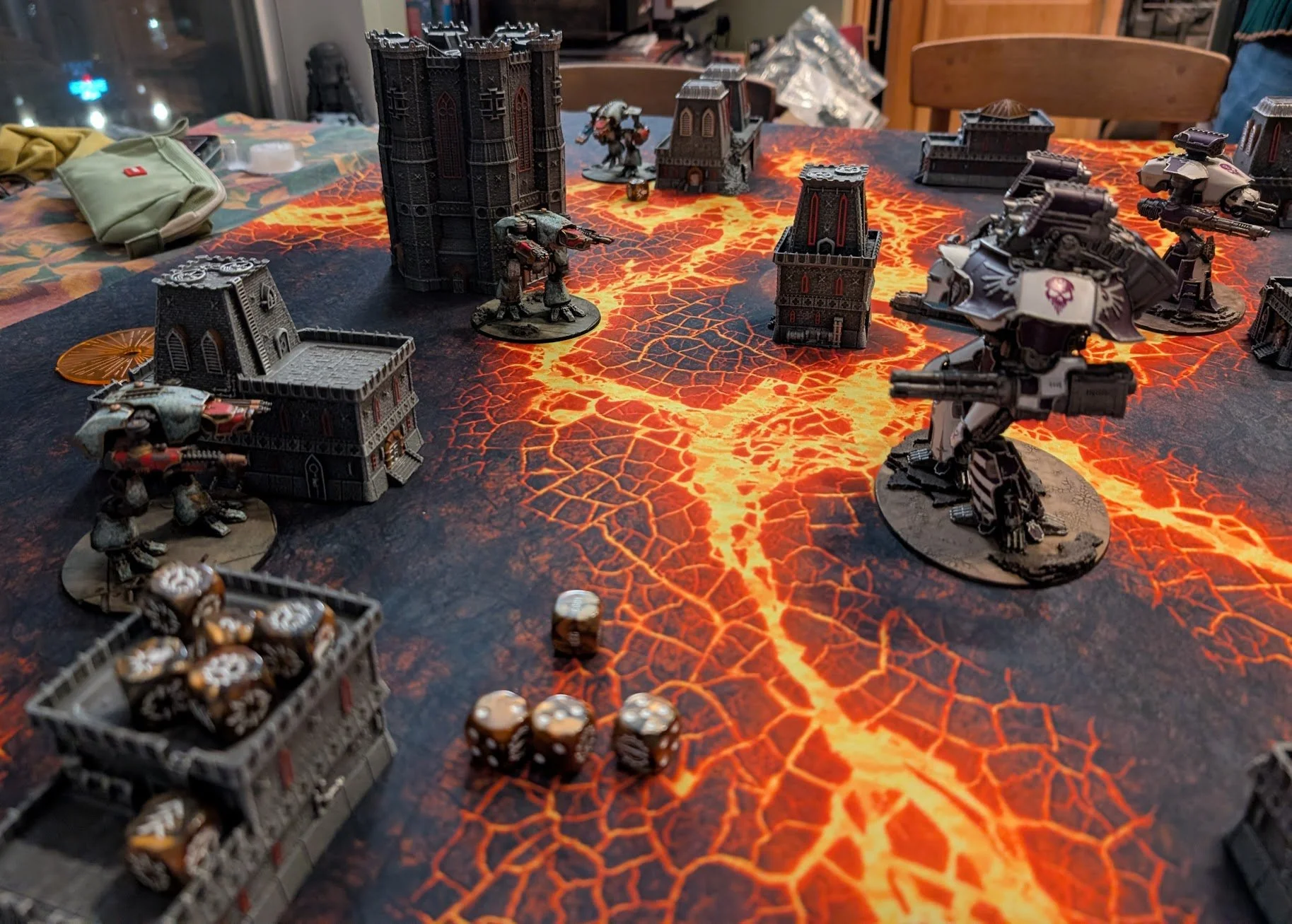 Adeptus Titanicus game on a glowing lava mat: white and purple titans on the right facing weathered green titans on the left among gothic ruins.