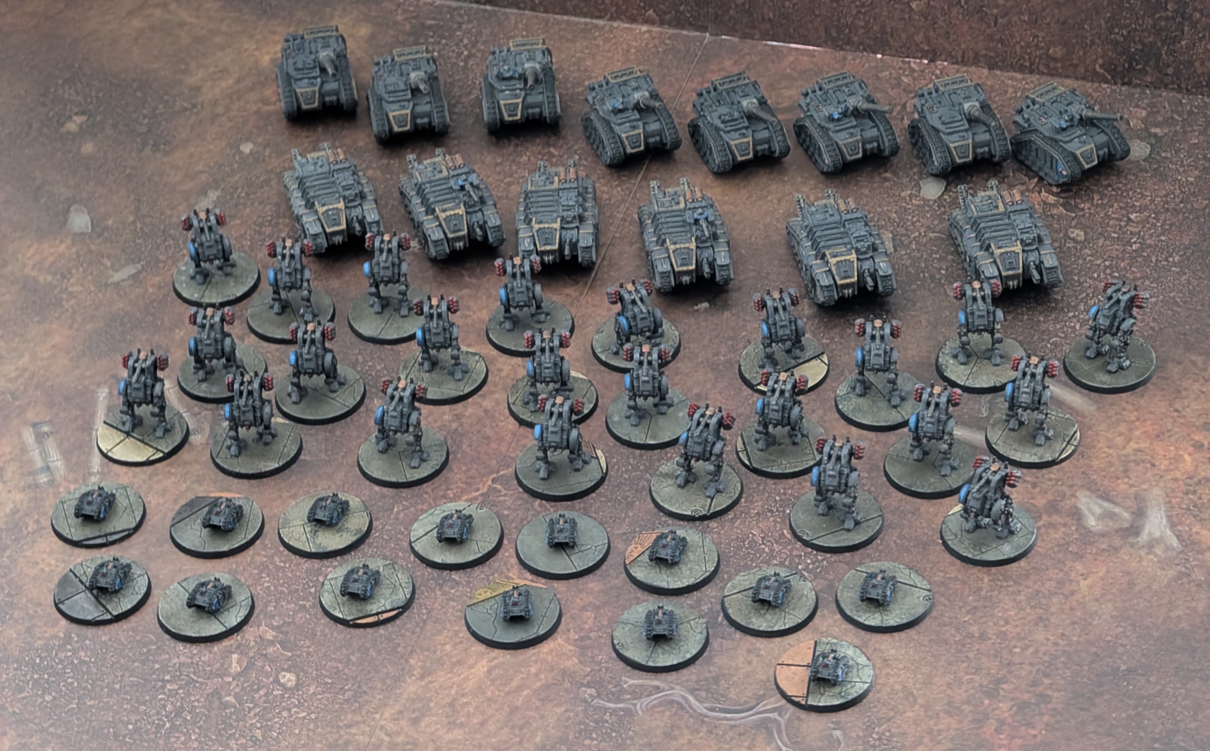 Rows of newly painted grey Solar Auxilia models: tanks and transports at the back, walkers in the middle, and small weapon platforms on round bases in front.